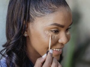 A woman applying concealer with a wand, smiling