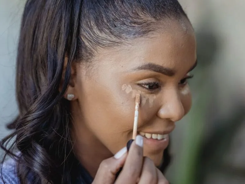 A woman applying concealer with a wand, smiling
