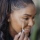 A woman applying concealer with a wand, smiling
