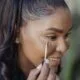 A woman applying concealer with a wand, smiling
