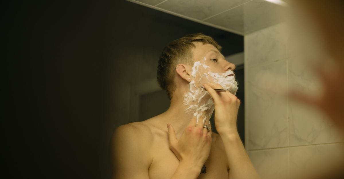 A man shaving his face at a mirror