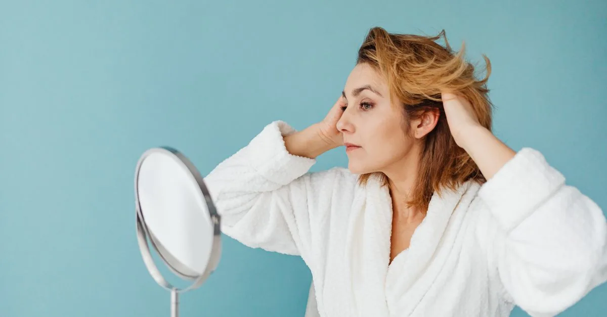 A woman examining her hair at a mirror