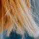 Frayed blonde hair ends against a teal background