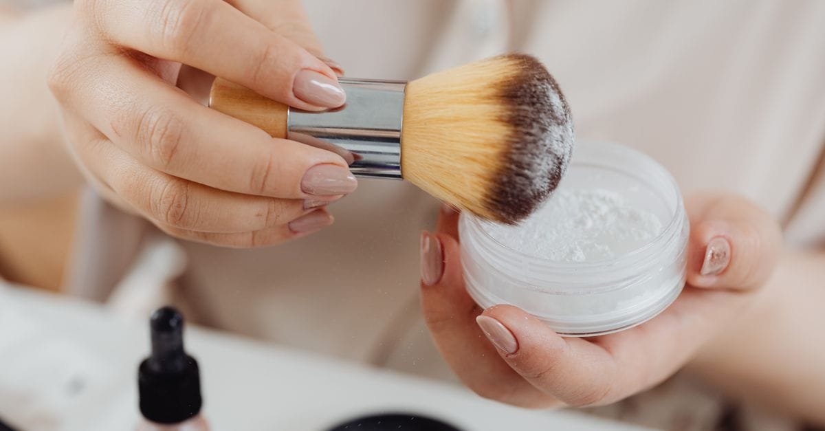 A powder brush resting on an open jar of loose powder