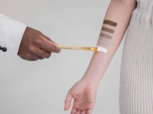 A makeup artist swatching foundation shades on a client&rsquo;s arm