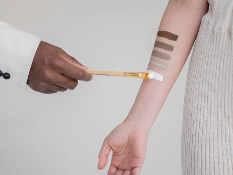 A makeup artist swatching foundation shades on a client&rsquo;s arm