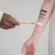 A makeup artist swatching foundation shades on a client&rsquo;s arm