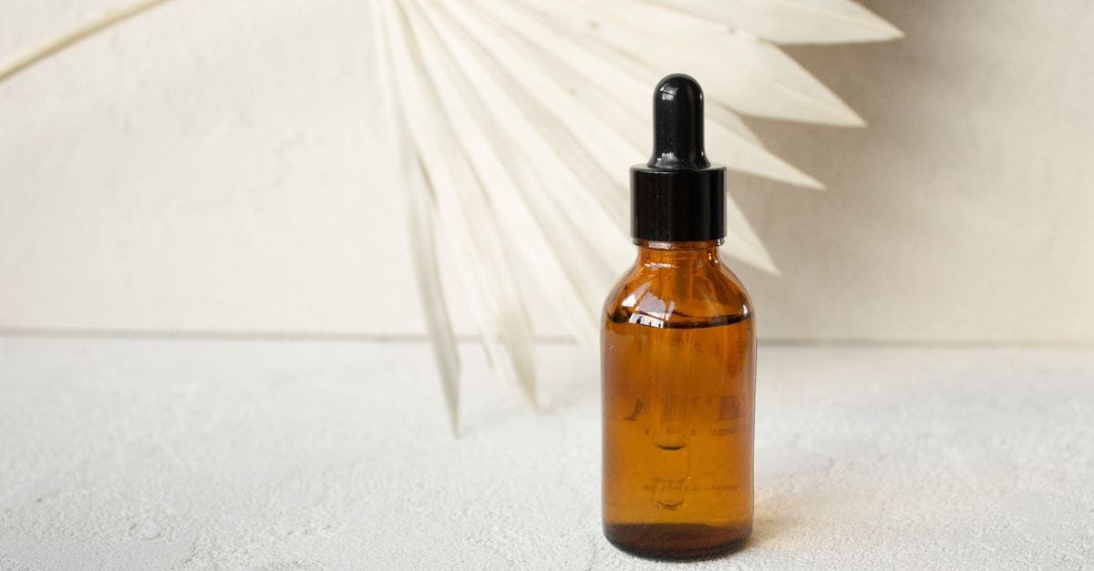An amber dropper bottle against a pale fan backdrop
